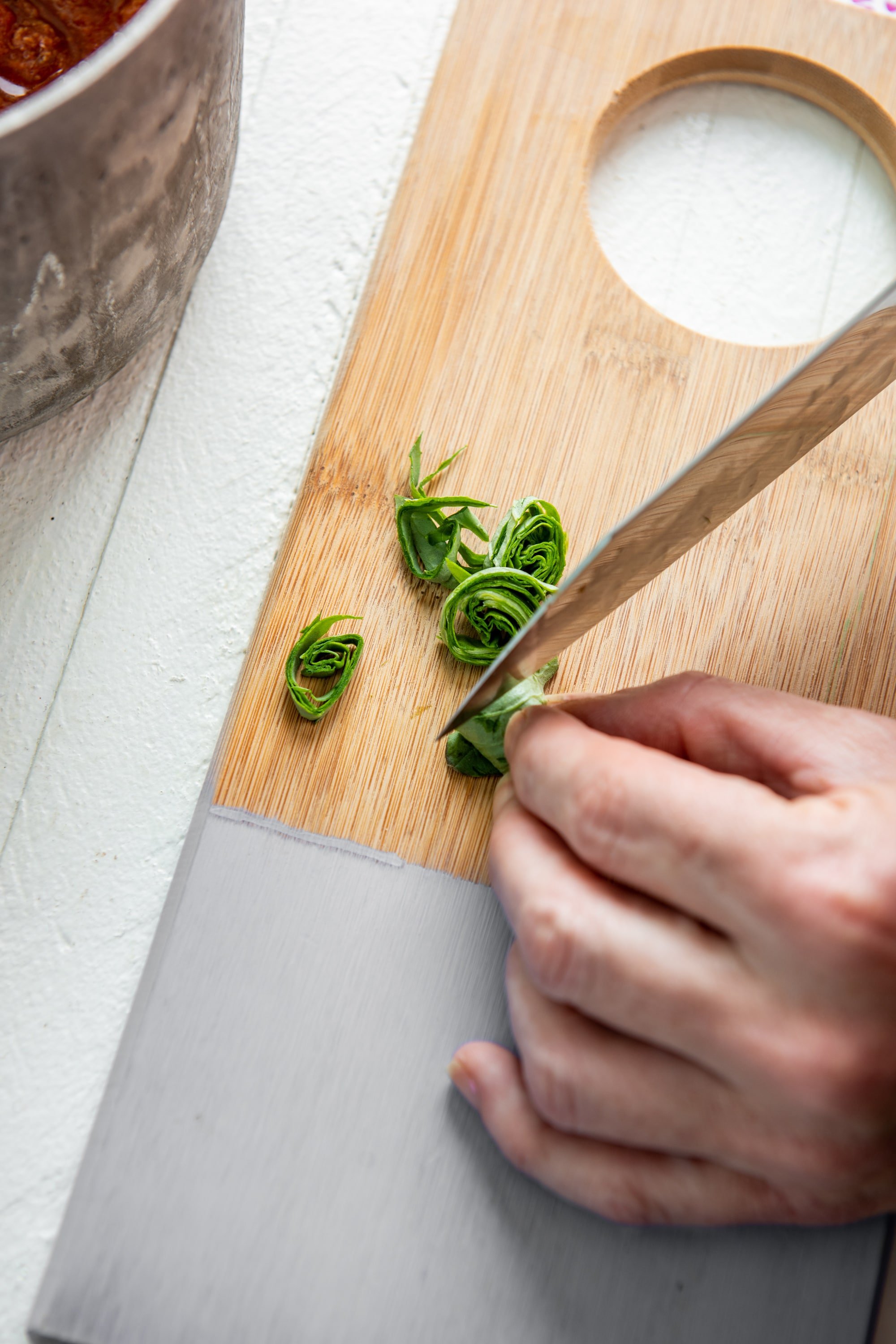 Woman cutting basil into chiffonade strips on a painted cutting board.