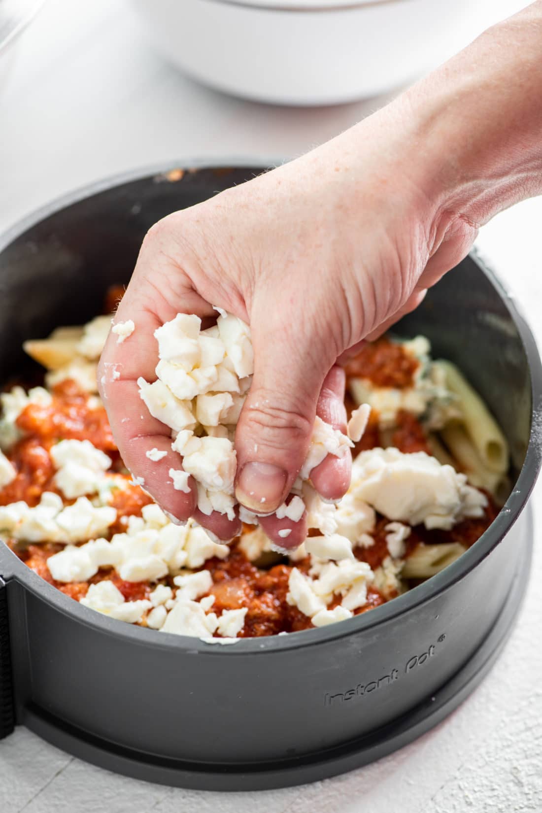 Woman adding mozzarella onto pasta and sauce in a pan.