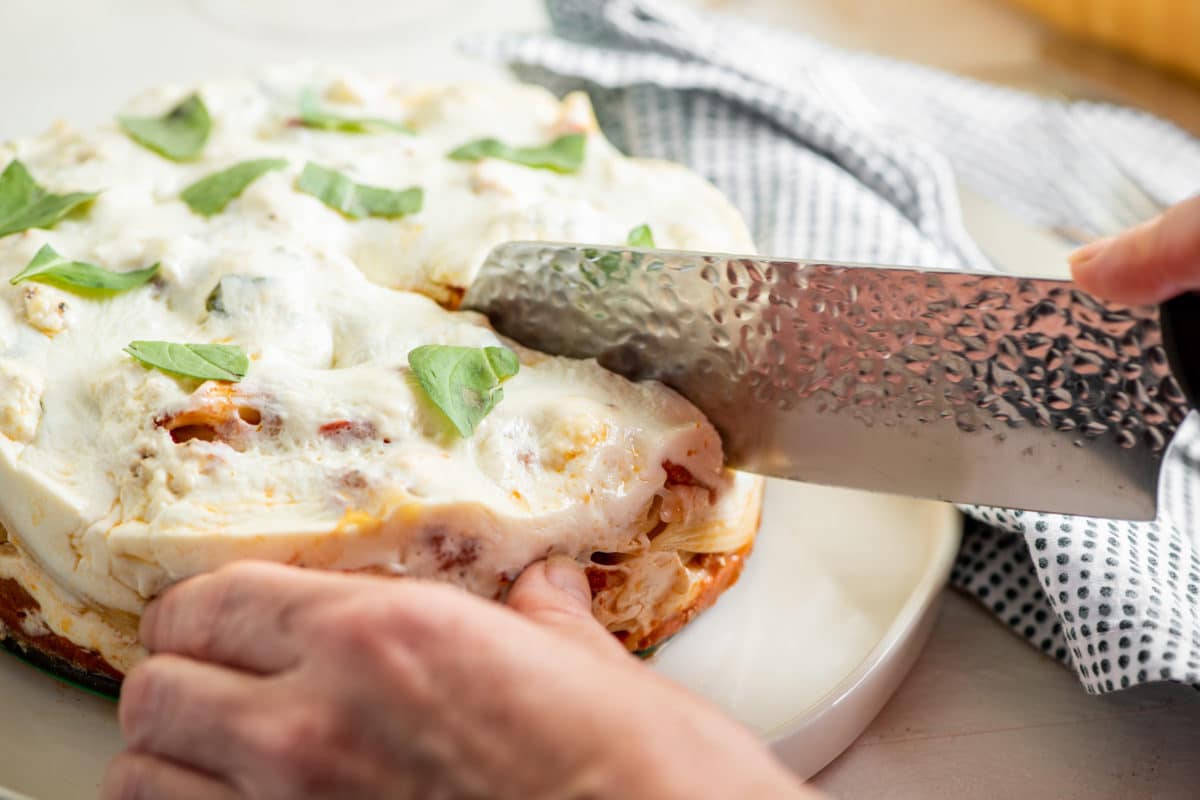 Woman slicing Ziti “Lasagna” with Bolognese Sauce.