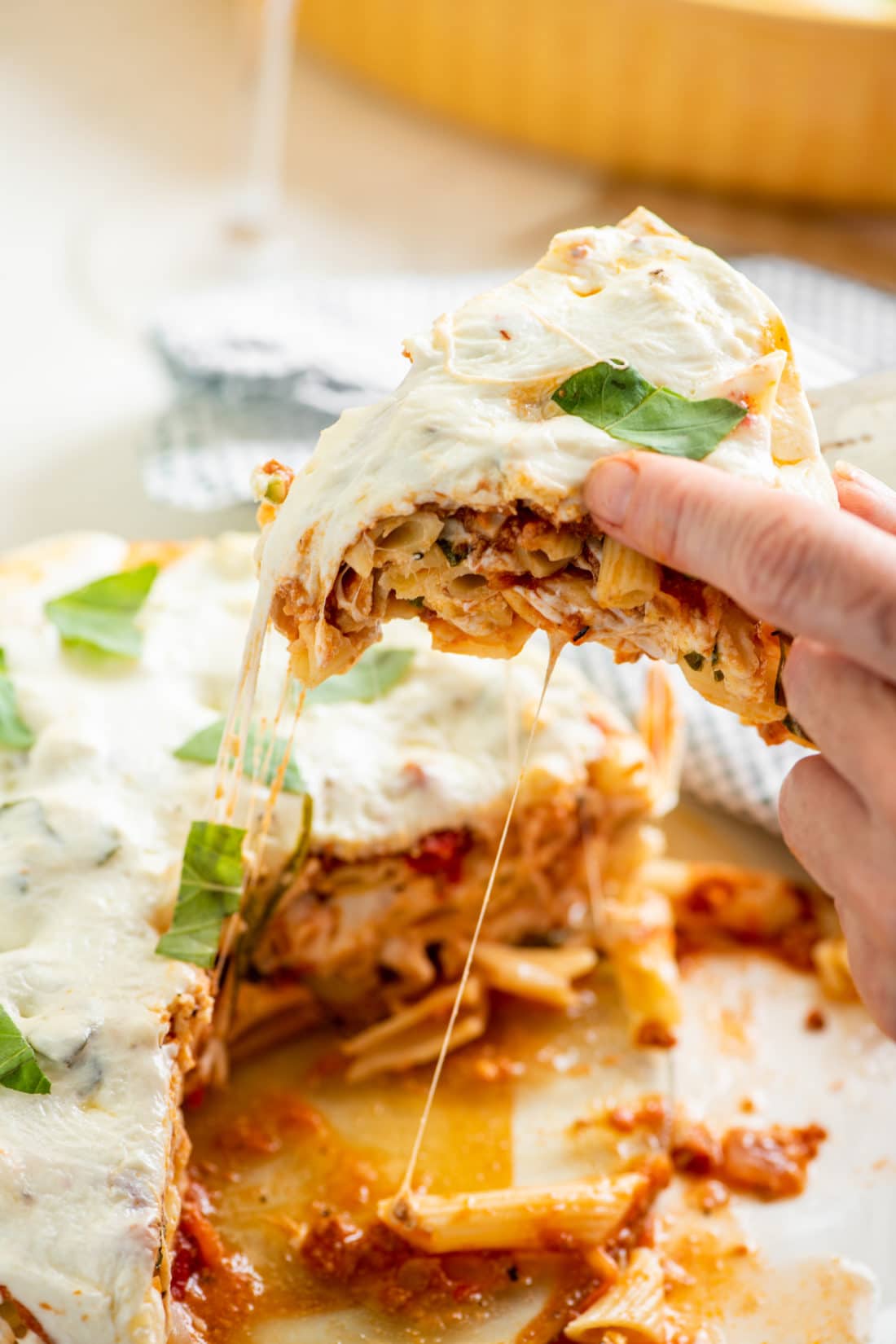 Woman removing a slice of Ziti “Lasagna” with Bolognese Sauce.