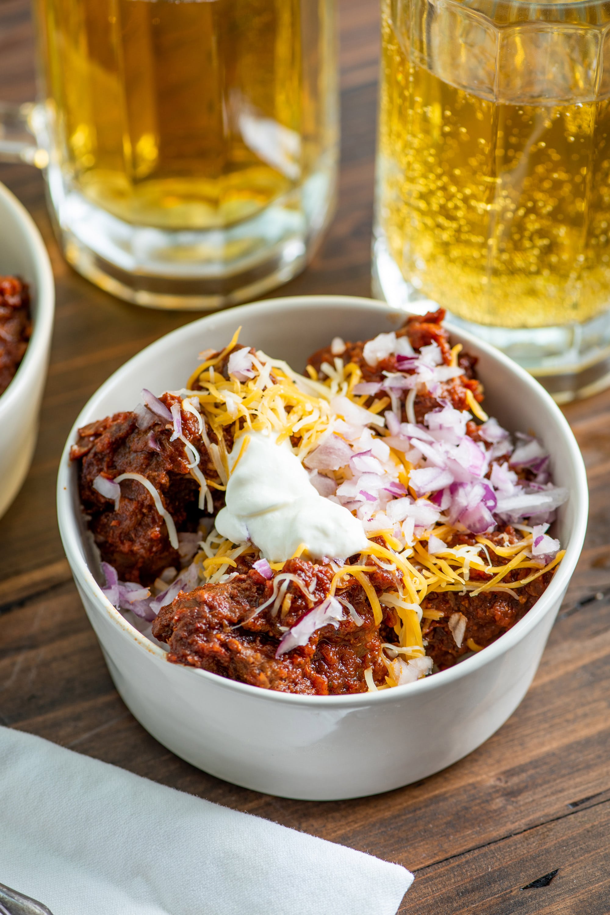 Bowl of Texas chili on table with glasses of beer.