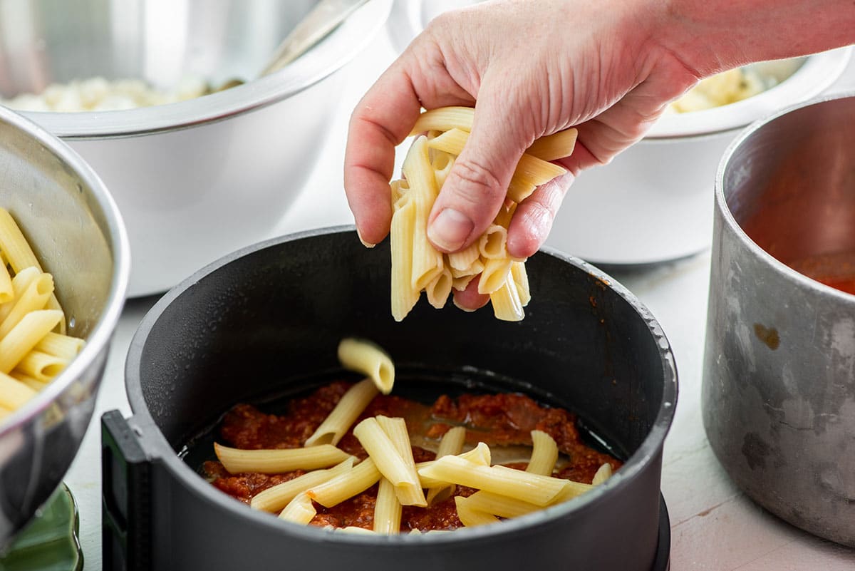 Woman adding ziti to pot of bolognese sauce.