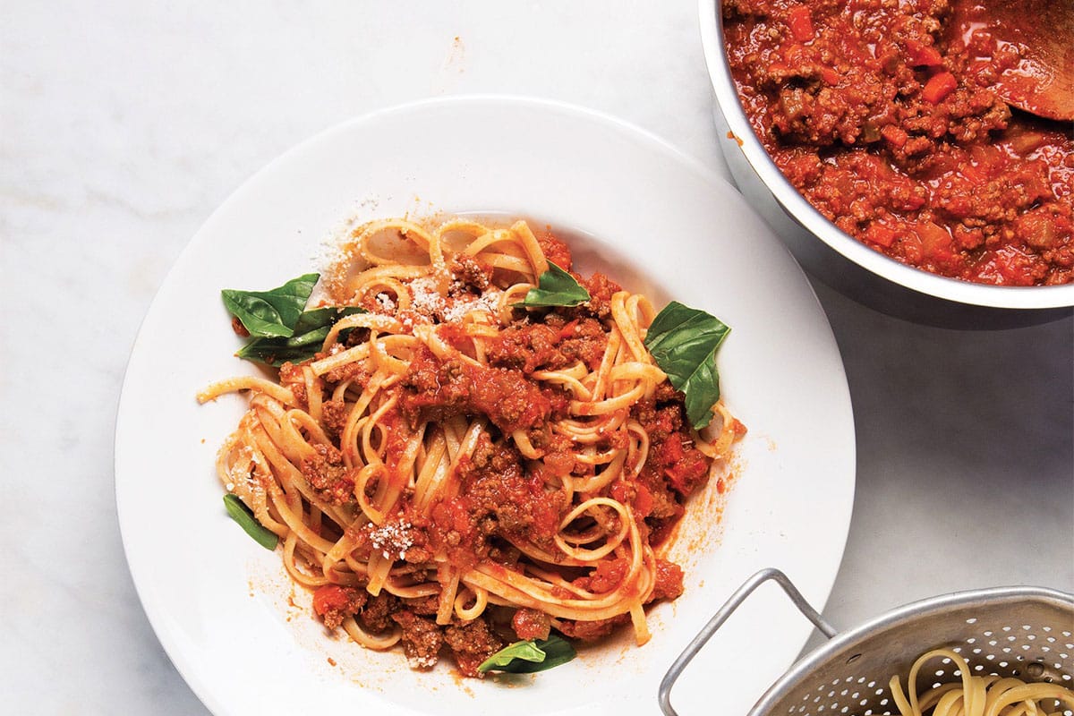 Bolognese sauce in pan and tossed with pasta on plate.