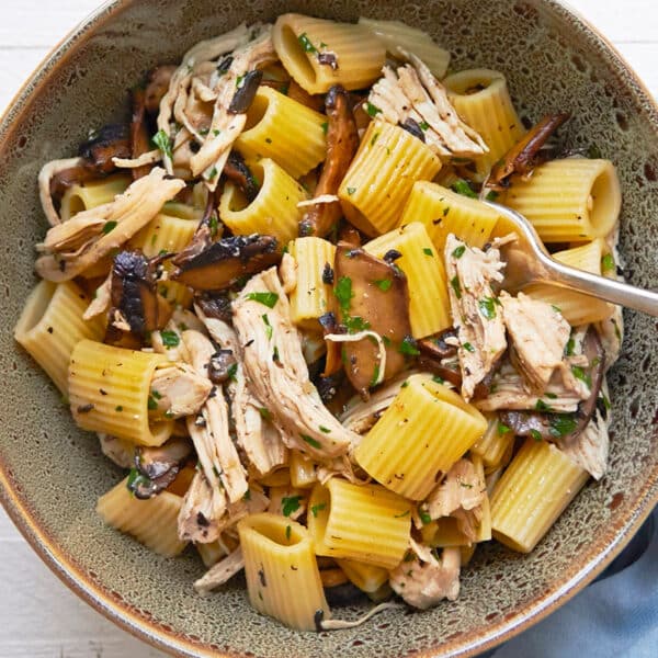 Simple chicken and pasta dish with Marsala wine sauce in brown bowl on table.