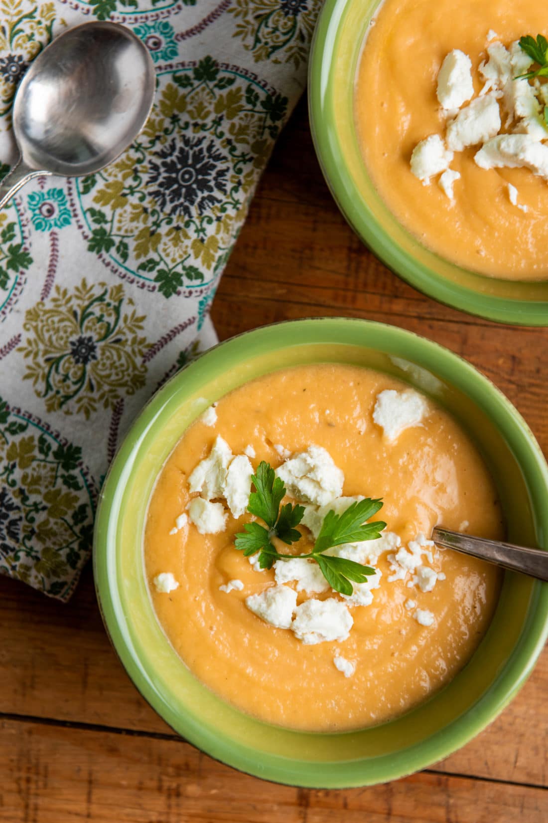 Green bowls of Creamy Rutabaga, Carrot and Parsnip Soup on a wooden table.