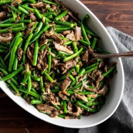 Sautéed green beans and mushrooms in serving dish with spoon.