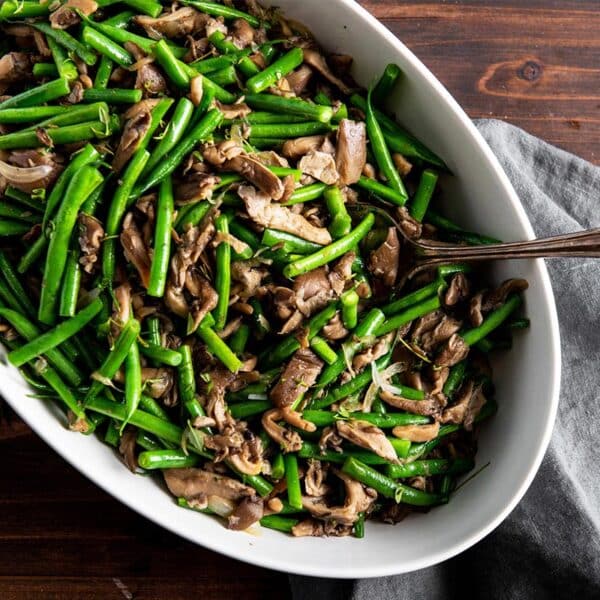 Sautéed green beans and mushrooms in serving dish with spoon.