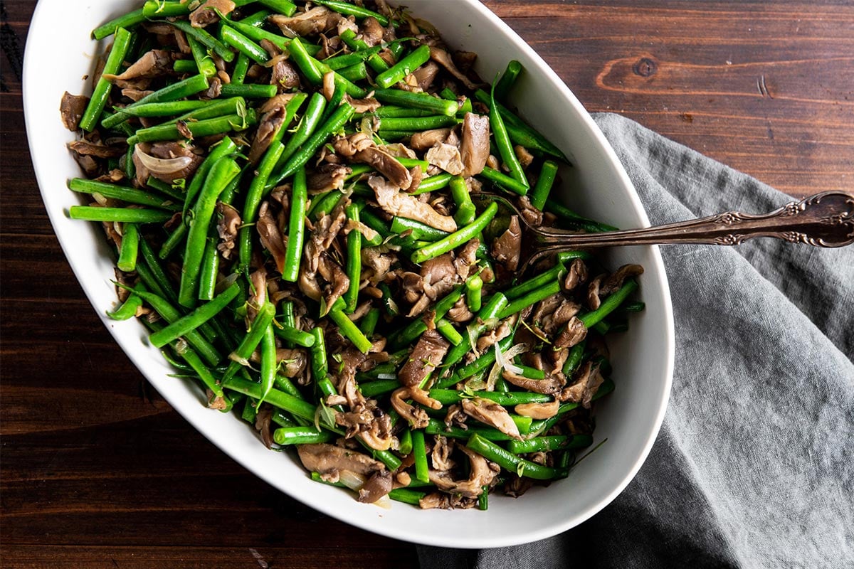 Sautéed green beans and mushrooms in serving dish with spoon.