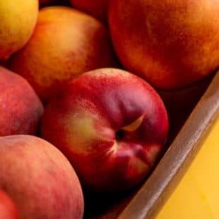 Wooden bowl of Peaches and Nectarines on a yellow surface.