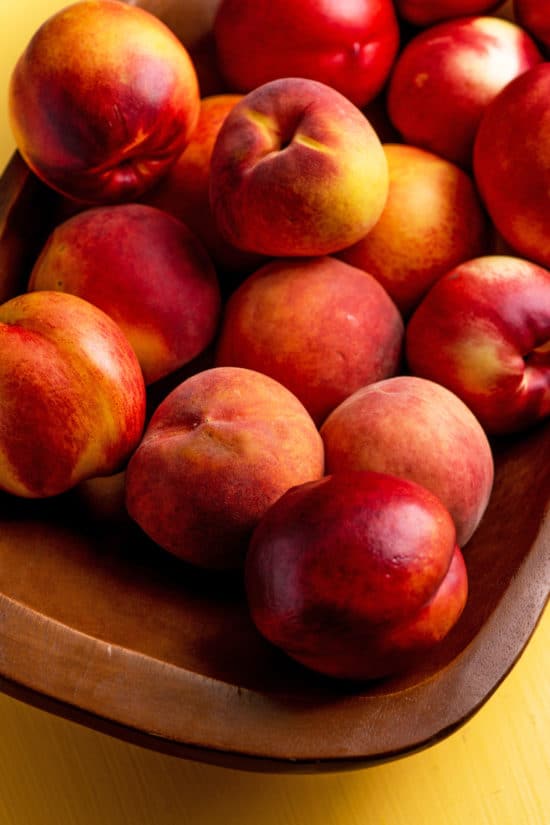 Peaches and Nectarines piled on a wooden bowl.