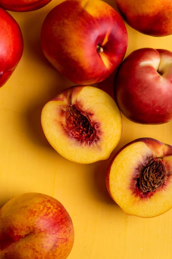 Peaches and Nectarines on a yellow surface, one of which is cut in half.