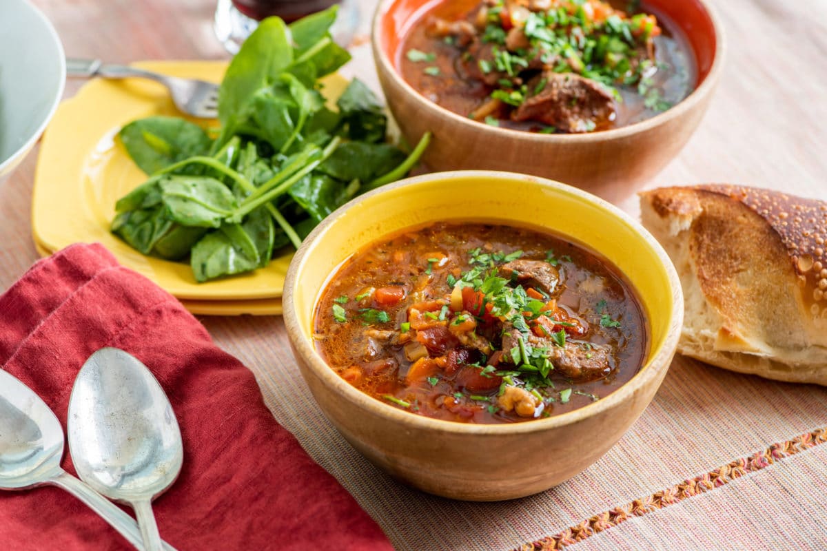 Bowls of Mediterranean Lamb Stew with a plate of spinach.