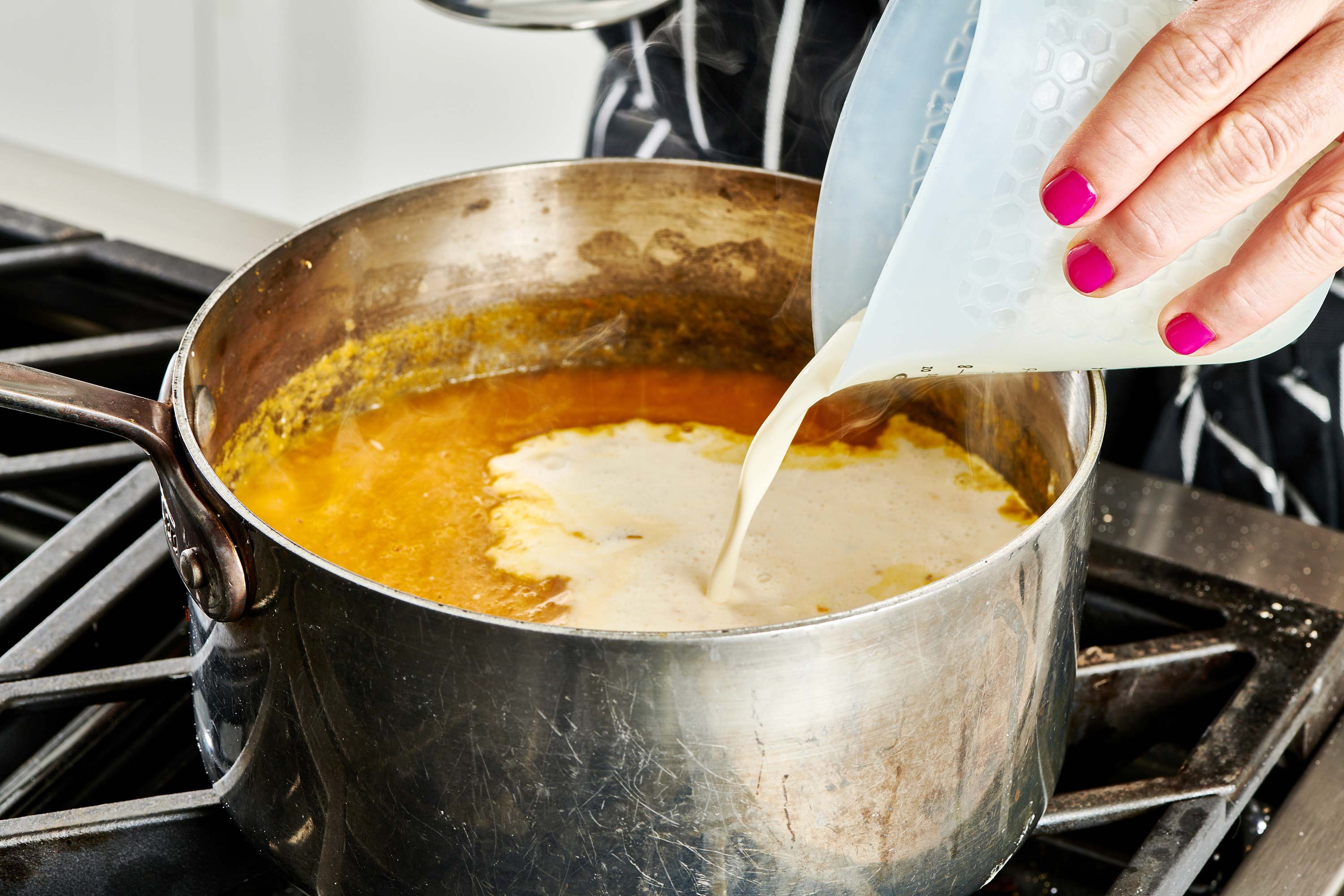 Woman pouring heavy cream into a pot of butternut squash puree.