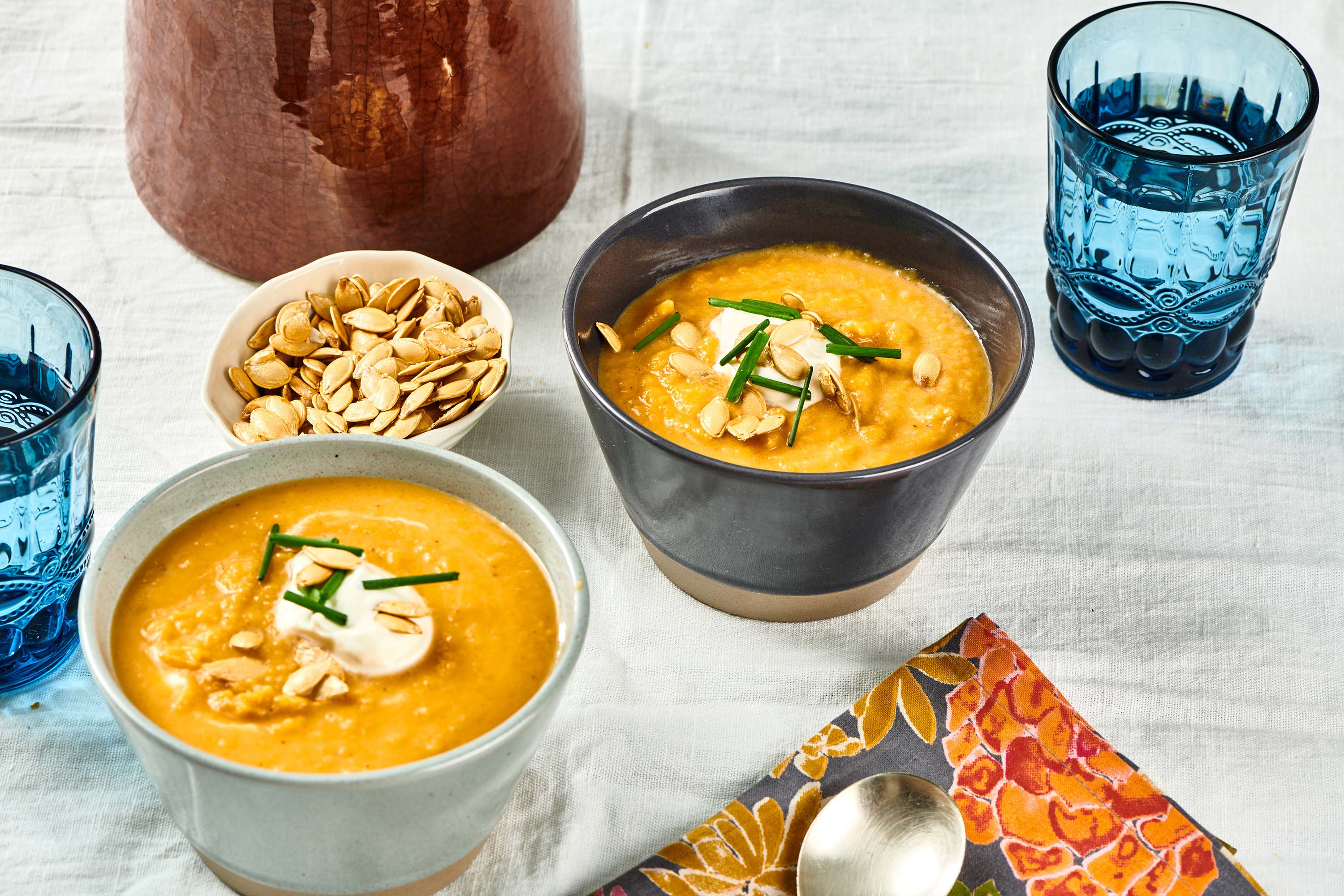 Two bowls of Roasted Butternut Squash Soup topped with chives, sour cream, and pumpkin seeds.