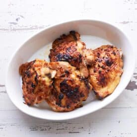 Baked Thai chicken thighs piled in white serving bowl on table.