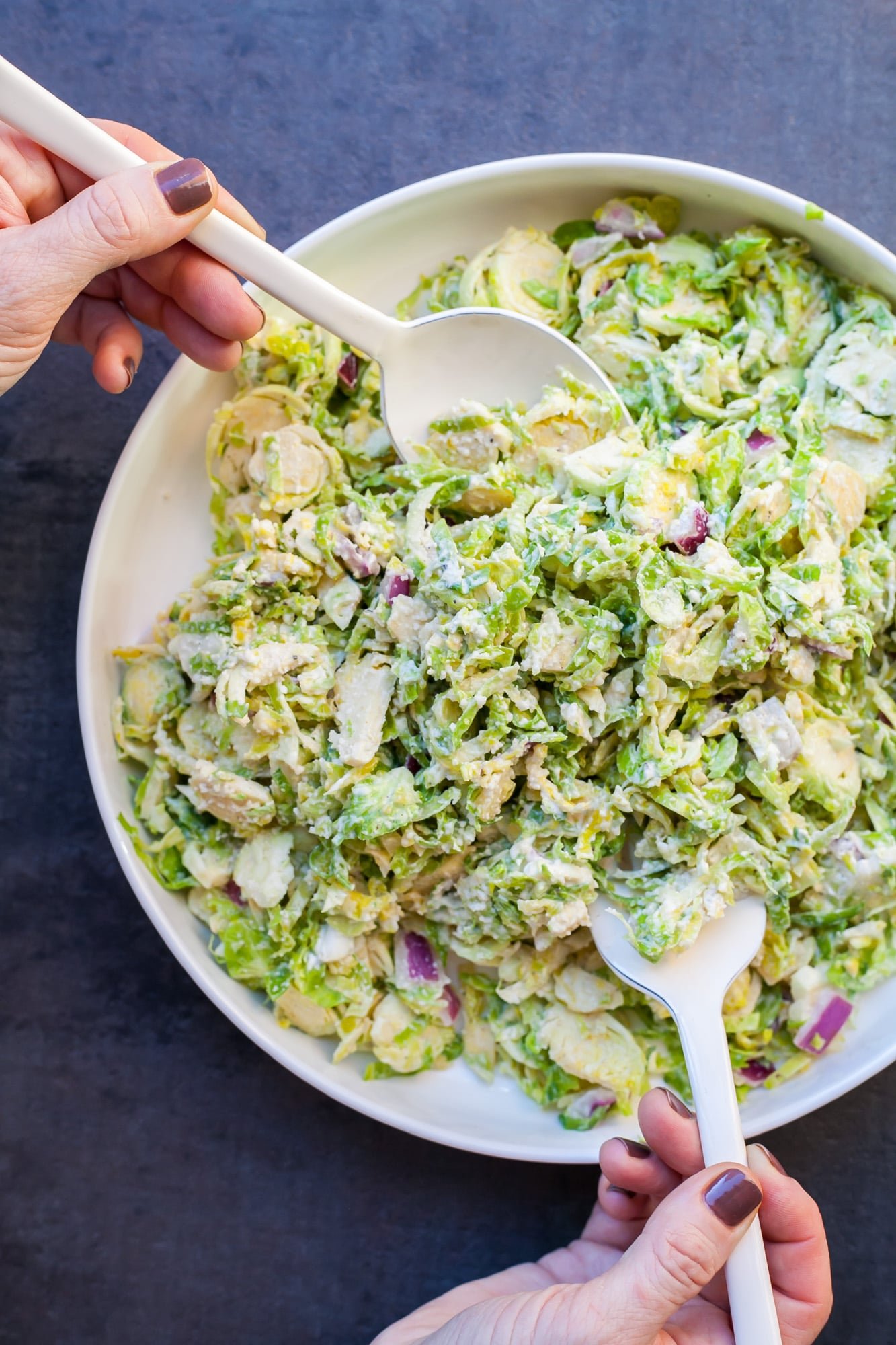 Woman tossing bowl of Creamy Brussels Sp.routs Slaw
