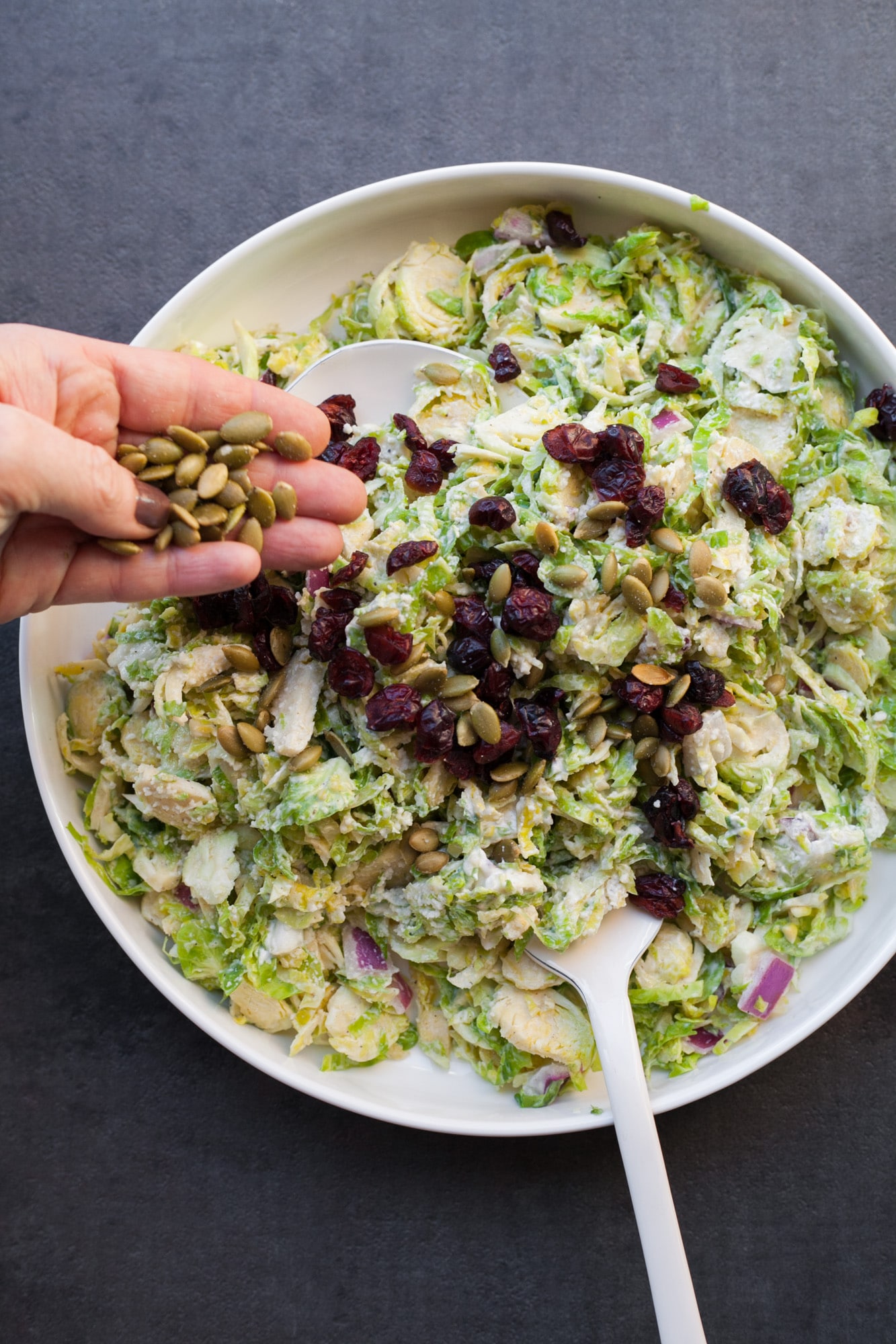 Woman sprinkles pepitas onto brussels sprouts slaw with dried cherries.