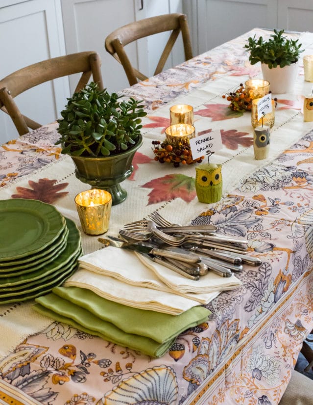 Table set with fall decorations, green plates, and utensils.