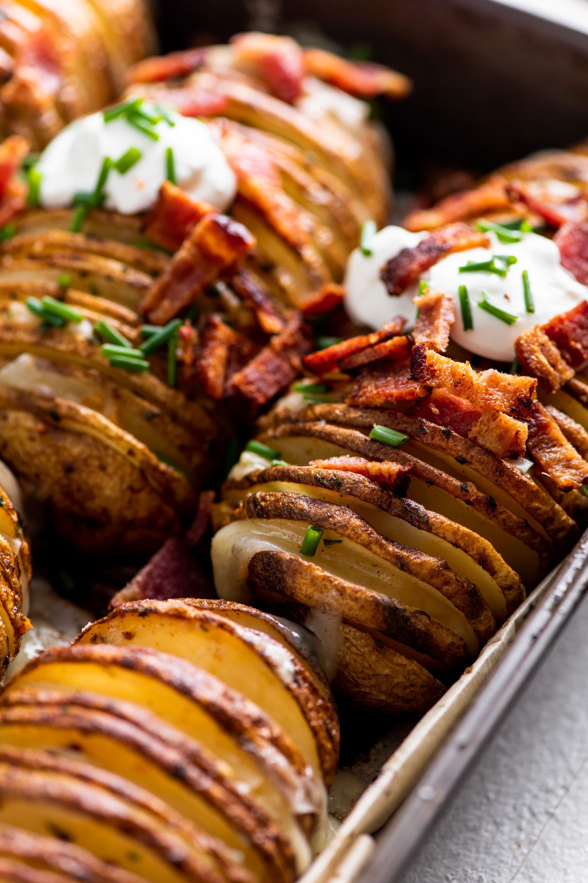 Hasselback potatoes with sour cream, chives and bacon in a pan.