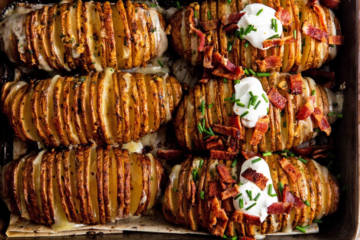 Cheesy Loaded Hasselback Potatoes, some of which have bacon and sour cream on top.