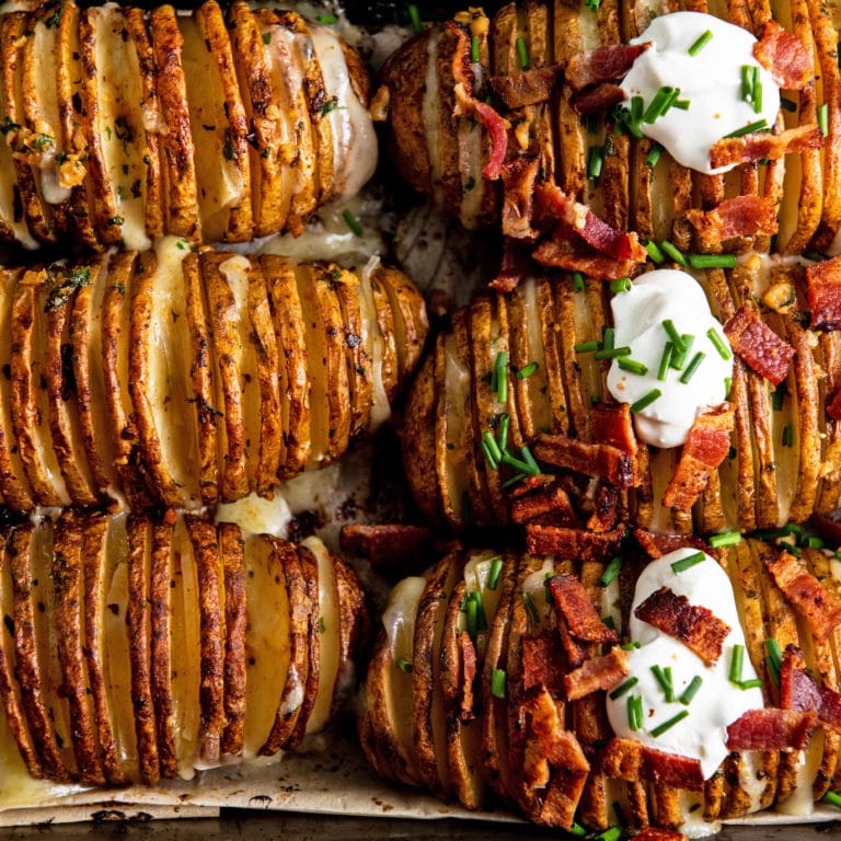 Cheesy Loaded Hasselback Potatoes, some of which have bacon and sour cream on top.