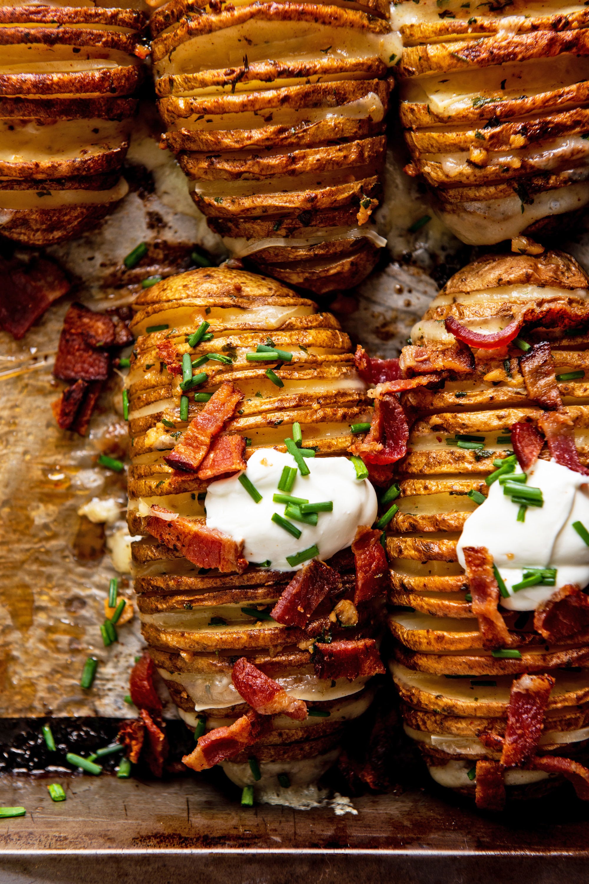 Lined baking sheet of Cheesy Loaded Hasselback Potatoes topped with bacon and sour cream.