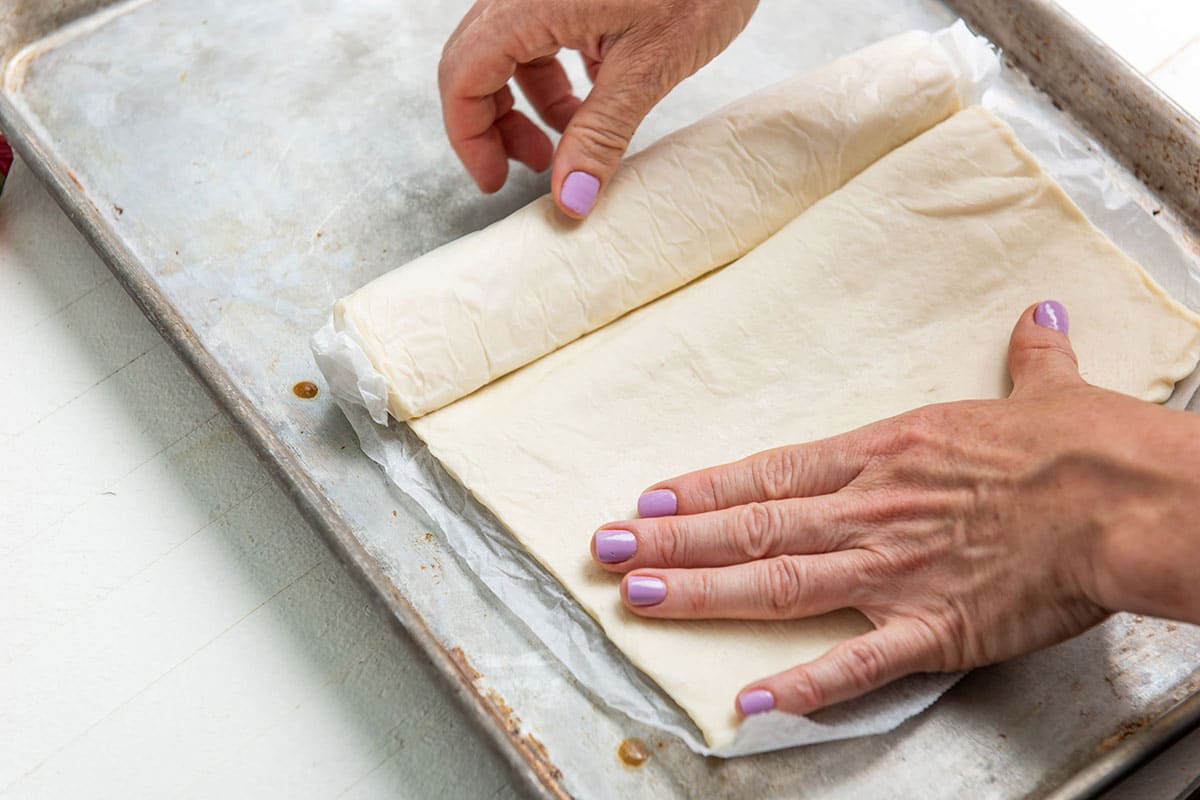 Woman rolling out sheet of store-bought refrigerated dough on pan.