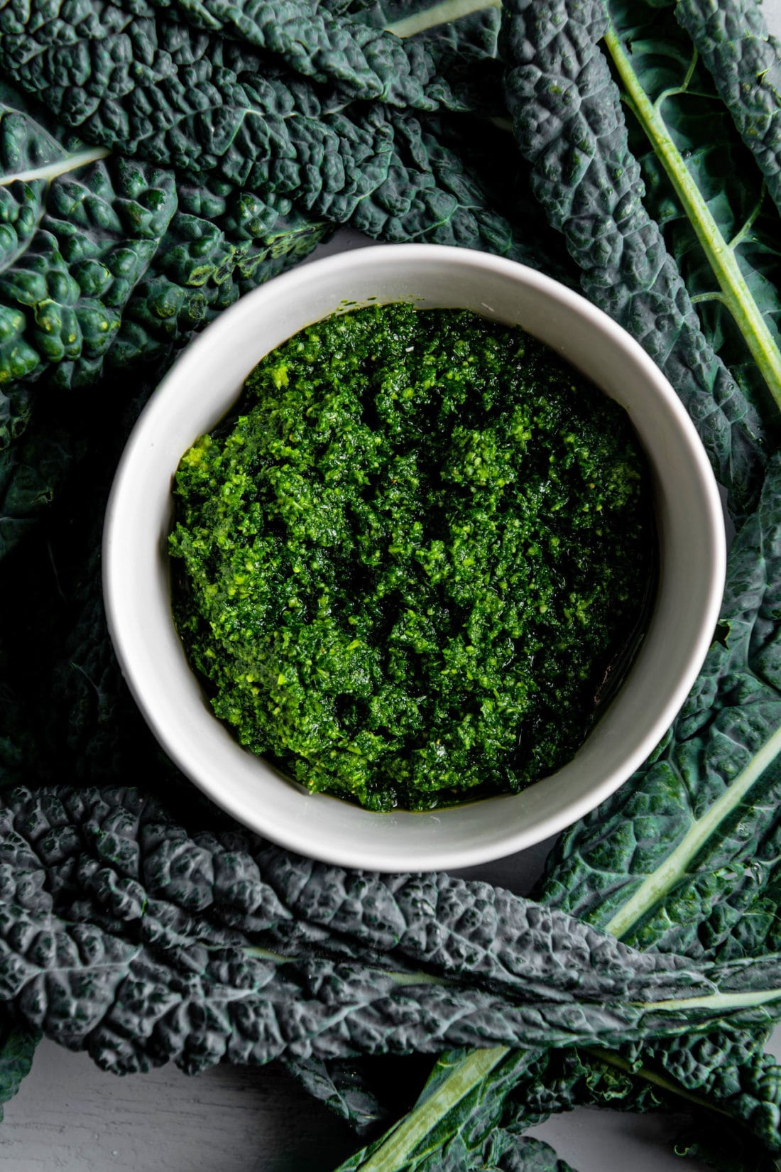 Bowl of Kale Pesto surrounded by kale leaves.