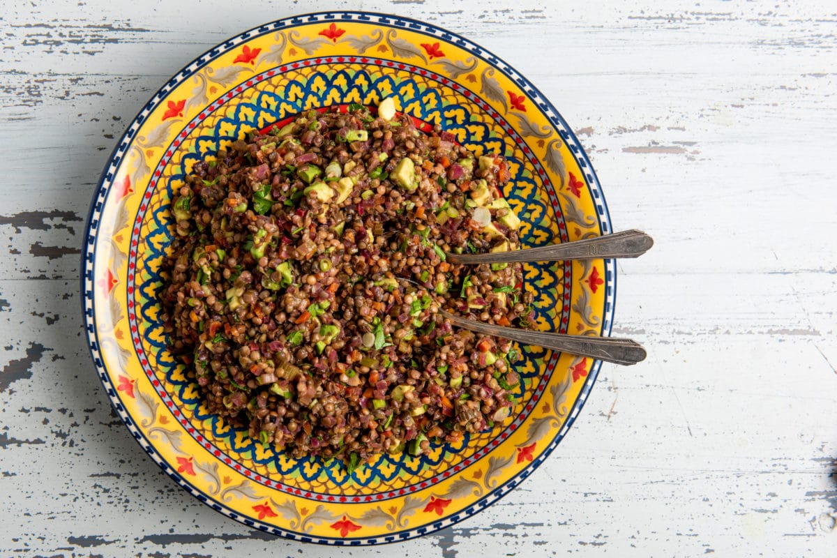 Two spoons in a colorful bowl of Lentil, Red Onion and Avocado Salad.