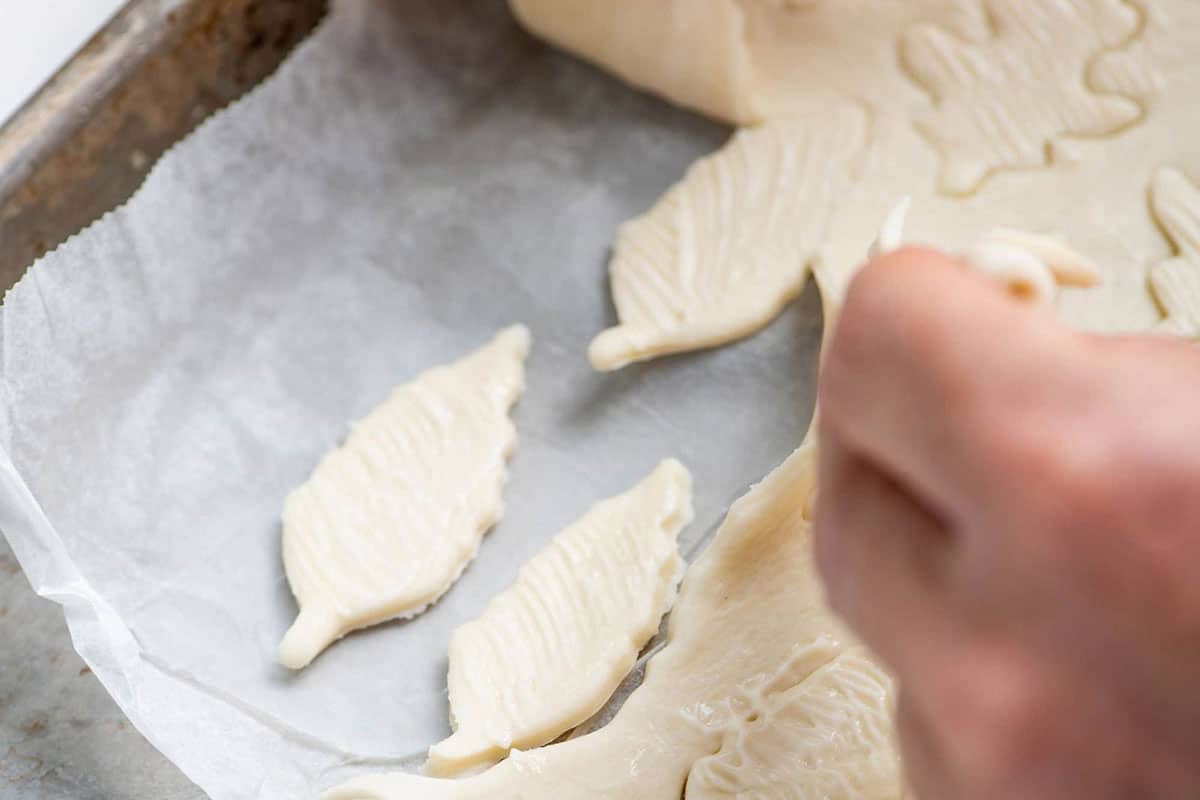Woman removing excess puff pastry from leaf cutouts.