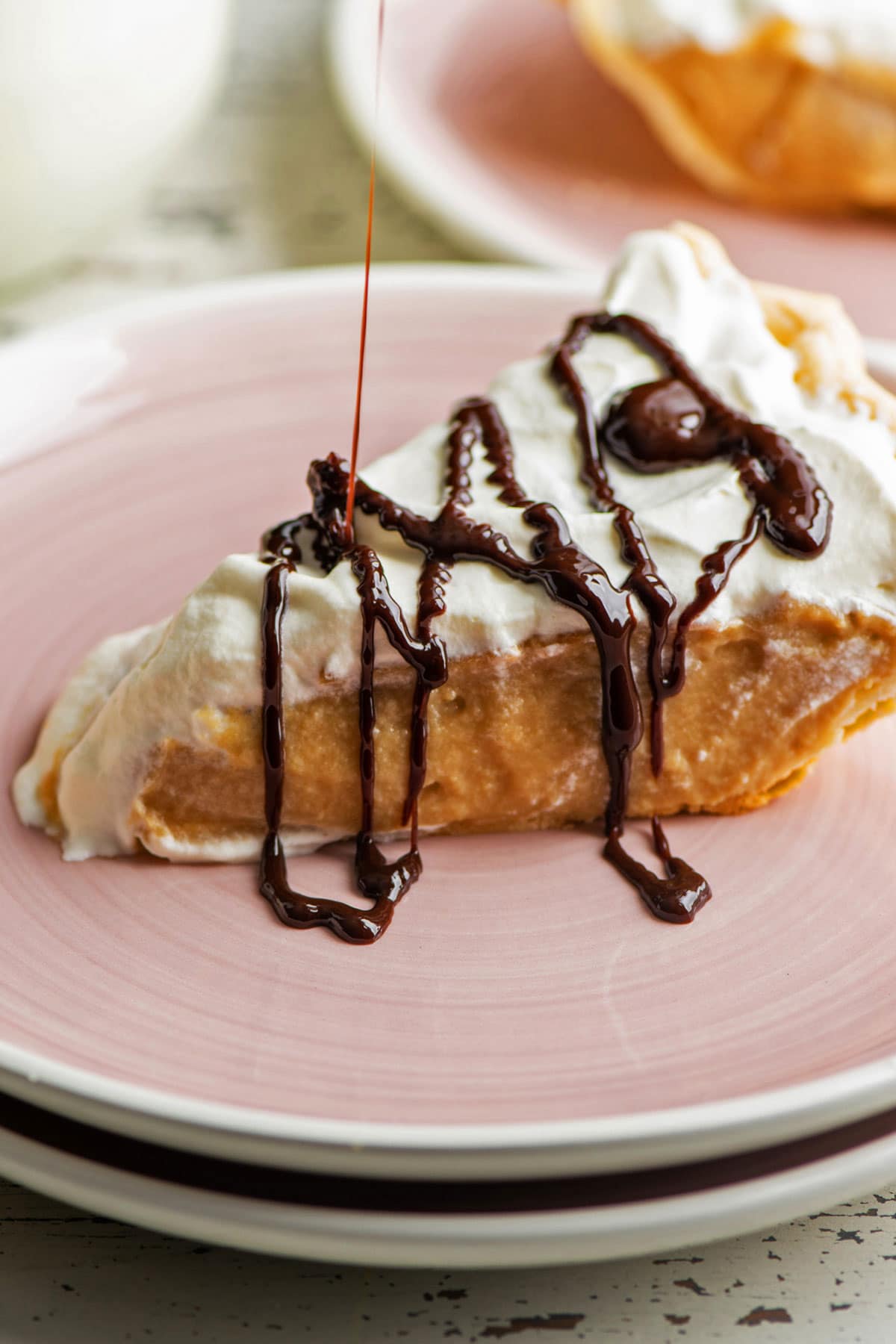Chocolate sauce drizzling onto a slice of Salted Butterscotch Pie.