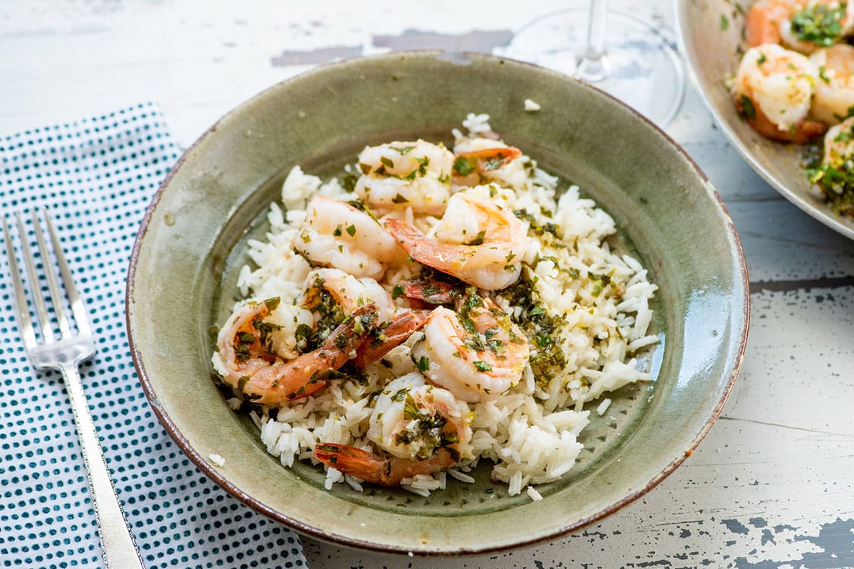 Green rice bowl with lemon shrimp on table.