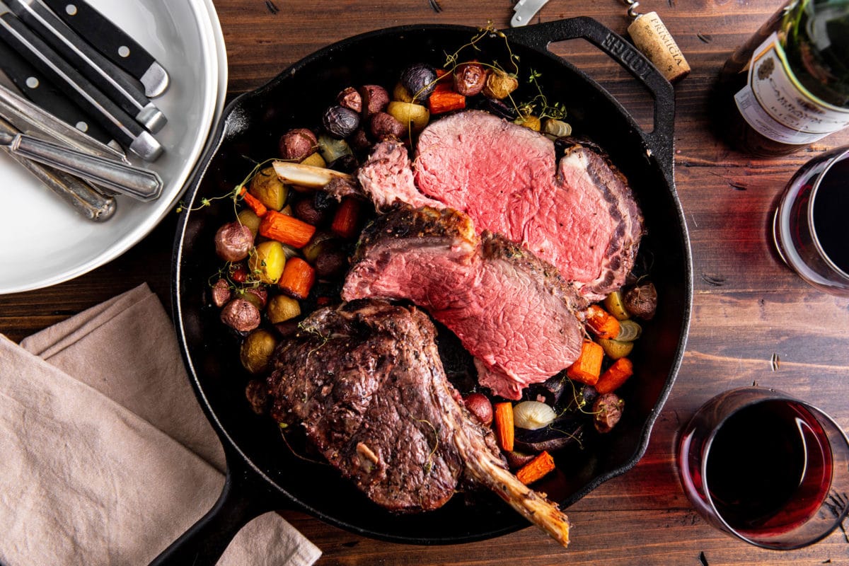 Skillet of Standing Rib Roast and vegetables on a table.