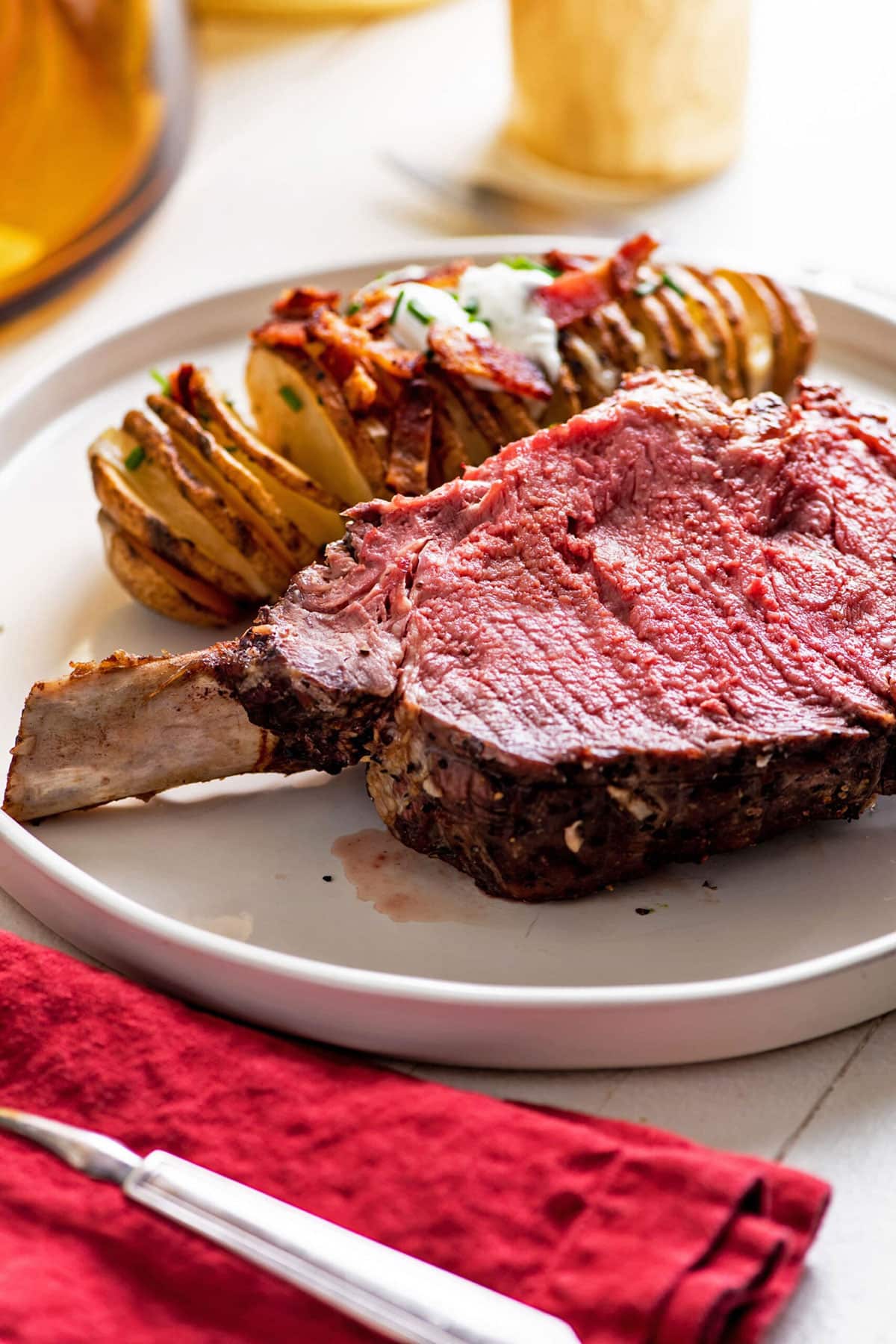 Slice of prime rib roast on plate with Hasselback potato.