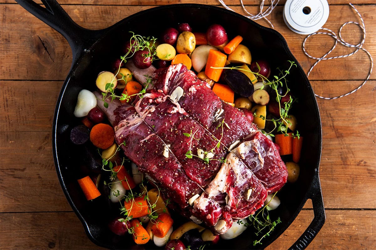 Raw Standing Rib Roast tied with twine in pan with vegetables.