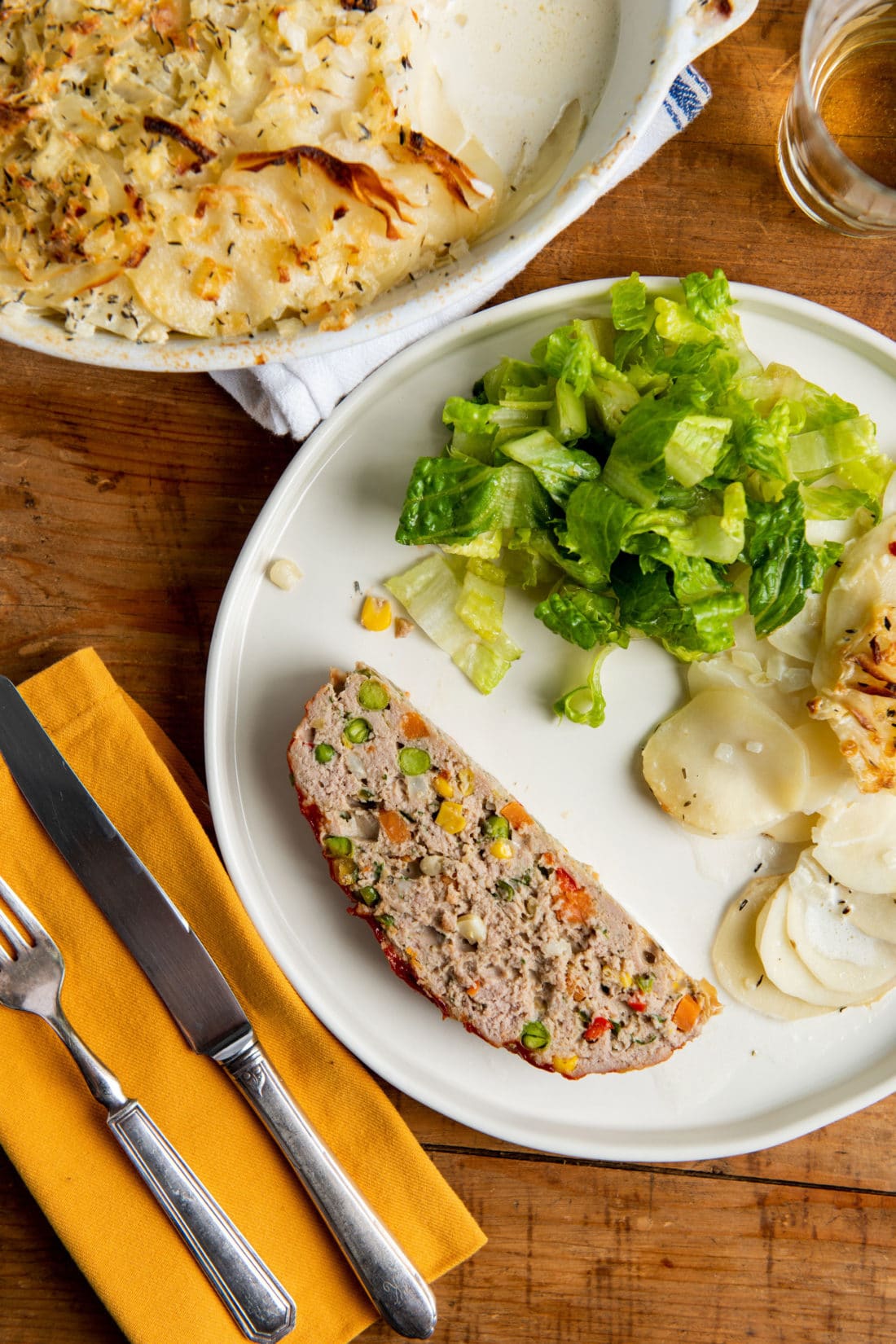 Slice of Vegetable Studded Turkey Meatloaf on a plate with potatoes and salad.