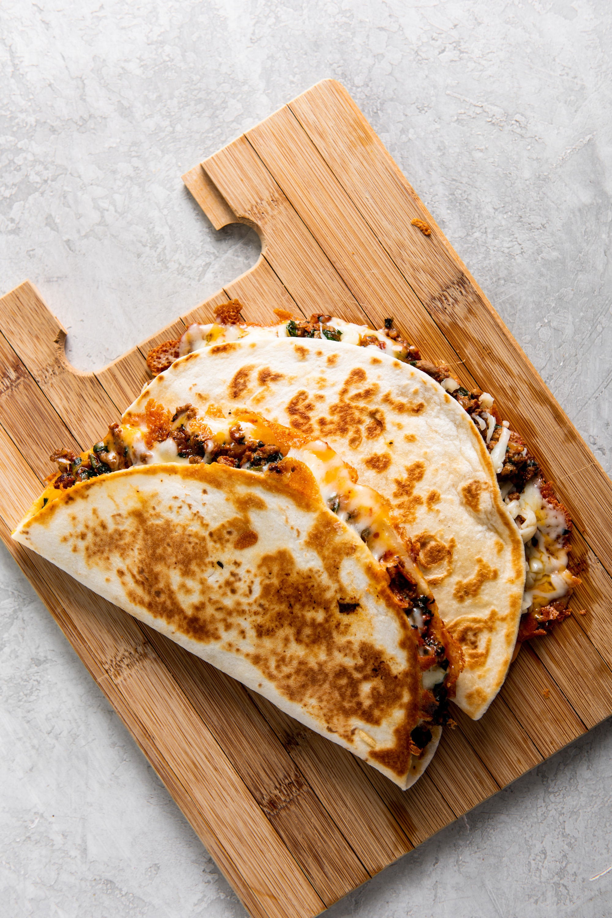 Two Cheesy Ground Beef Quesadillas stacked on cutting board.