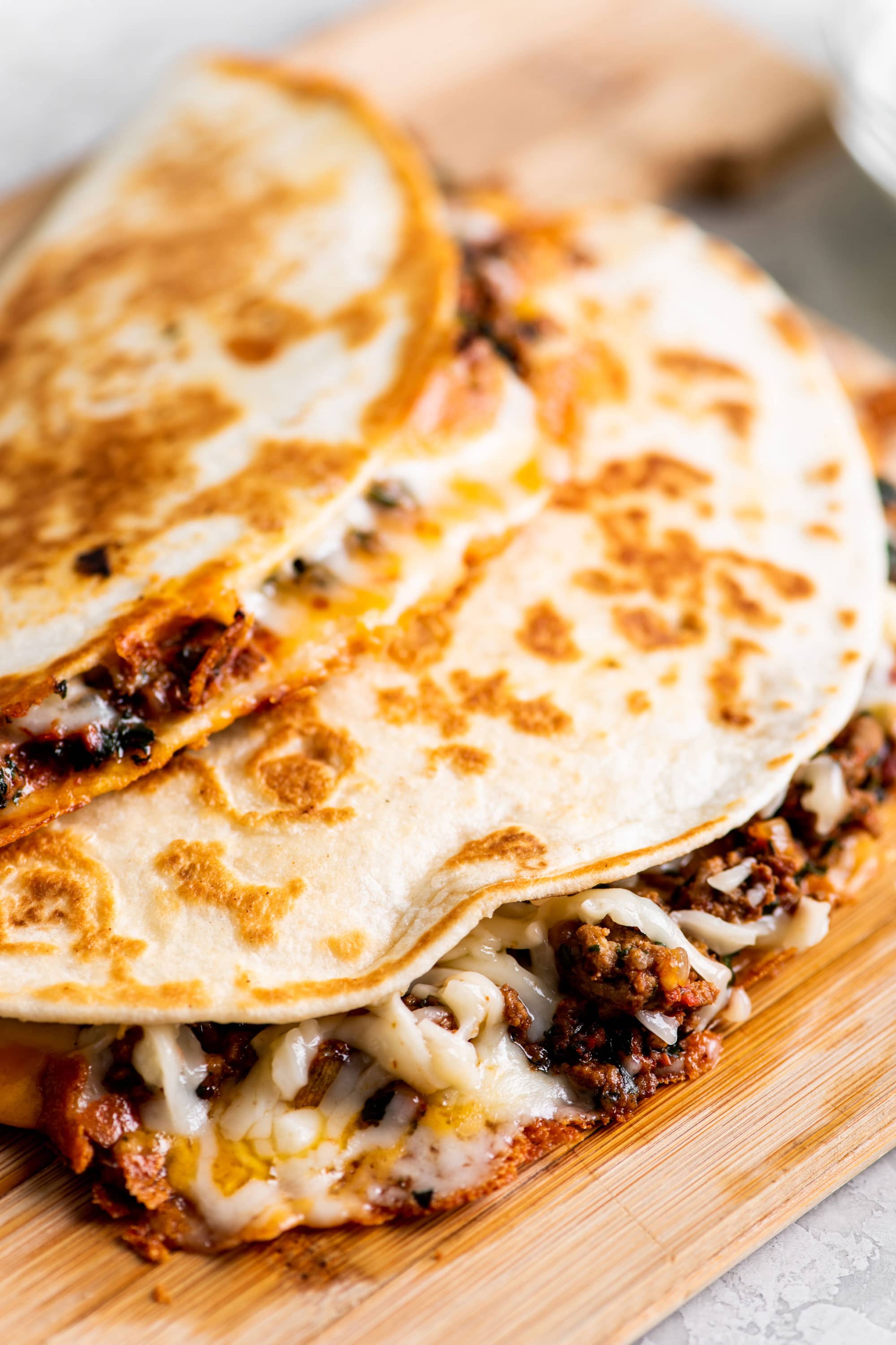 Stack of cheesy beef quesadillas on cutting board.