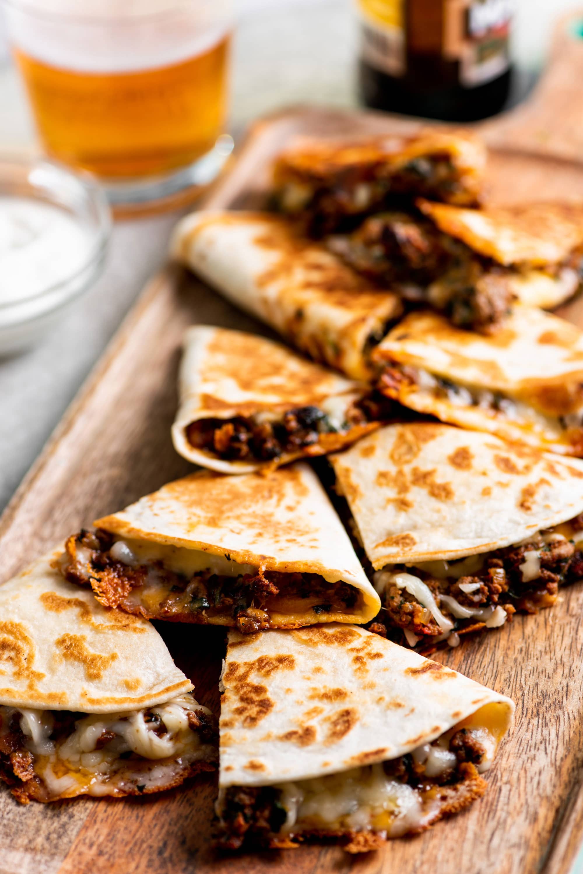 Cheesy Ground Beef Quesadillas on cutting board alongside glass of beer.