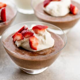 Chocolate mousse with strawberries and whipped cream in three serving dishes on table.