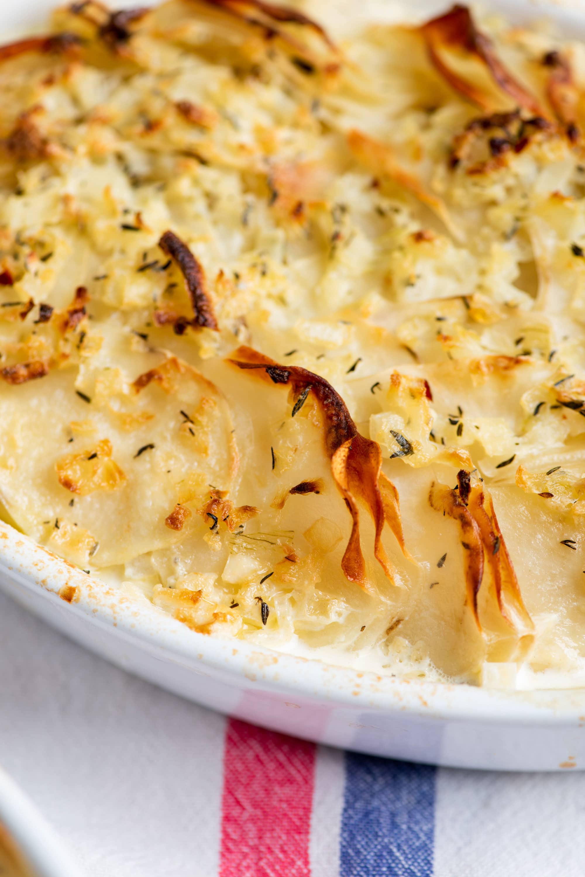 Creamy Scalloped Potatoes with crispy top in white baking dish.