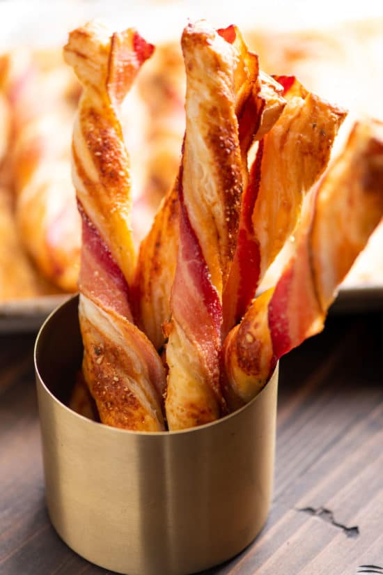 Cup holding several Herbed Cheesy Puff Pastry Bacon Straws.