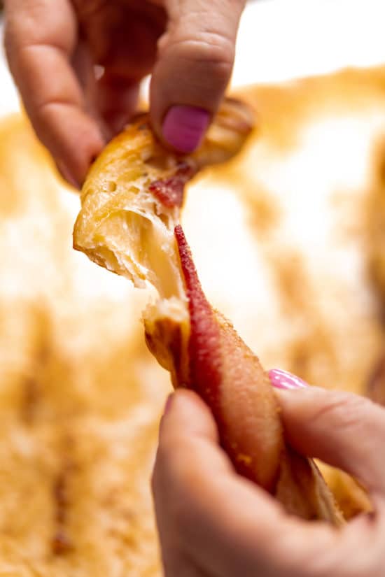 Woman pulling apart an Herbed Cheesy Puff Pastry Bacon Straw.