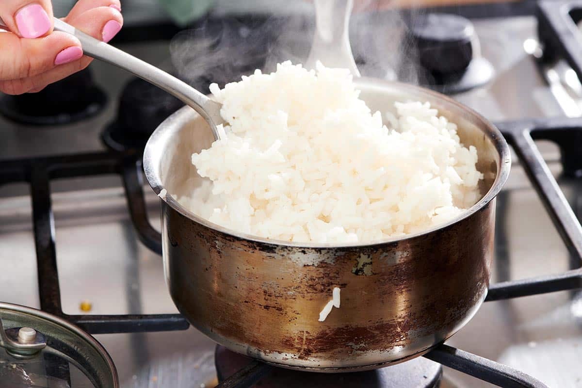 Fluffing cooked white rice in pan on stove with fork.