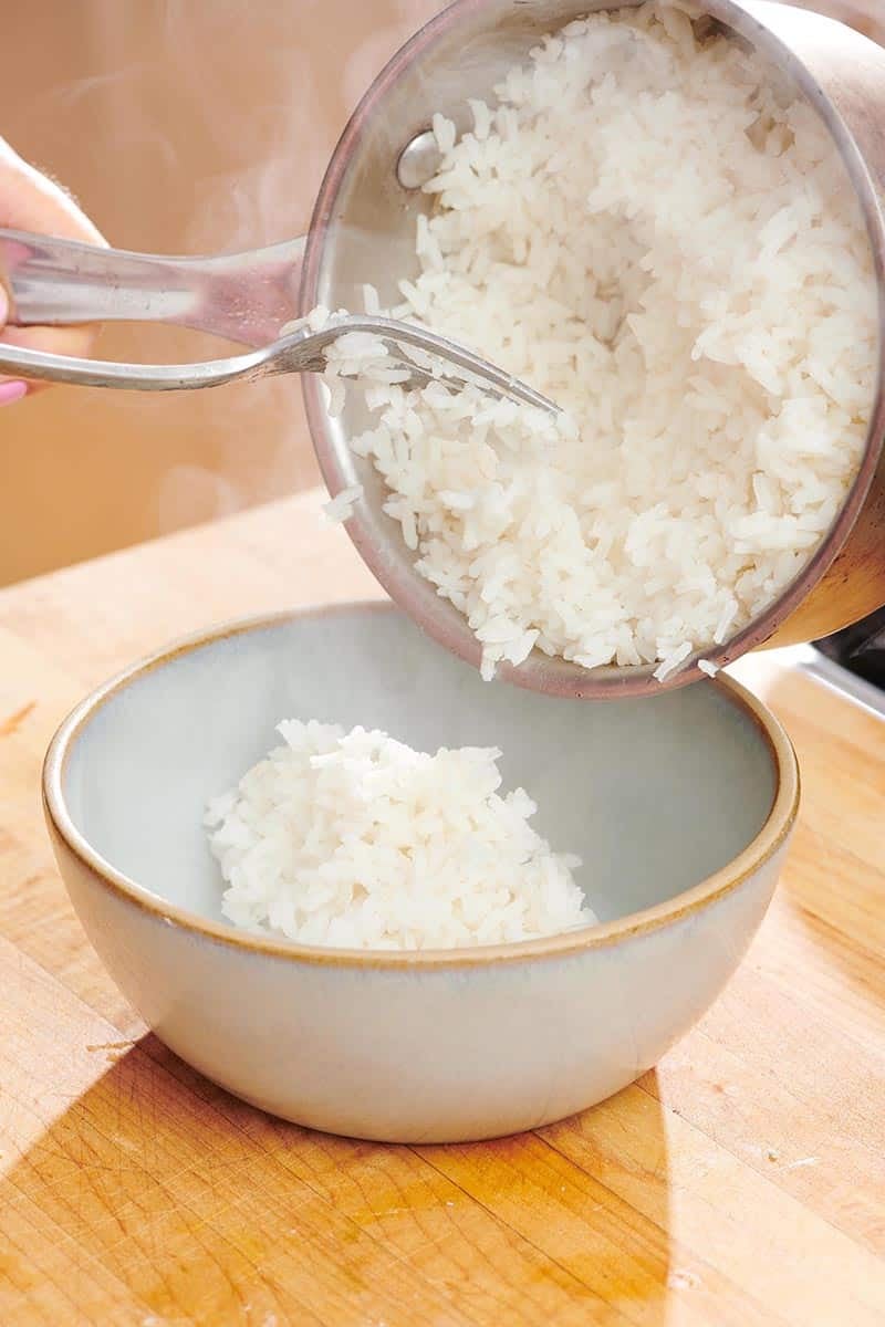 Pouring cooked white rice from pan into serving bowl.