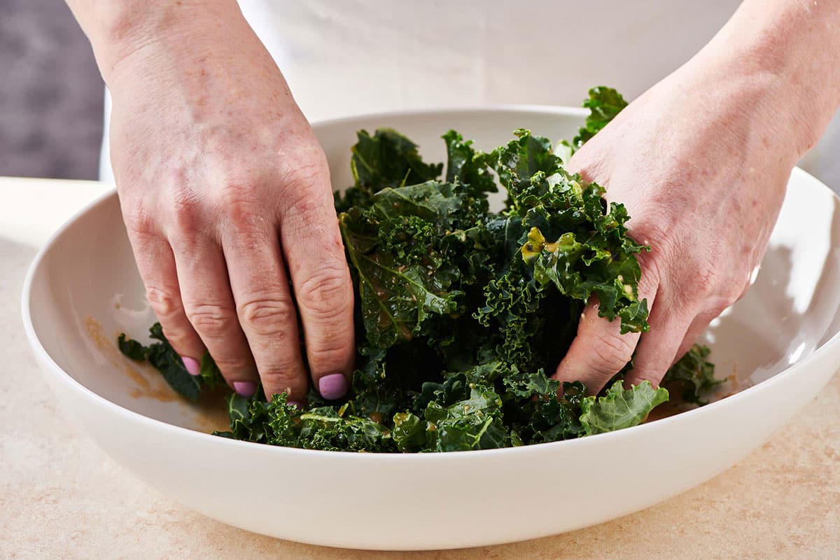 Woman tearing kale in white bowl.