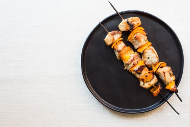 Two Mustard and Maple Pork Kebabs on a black plate.