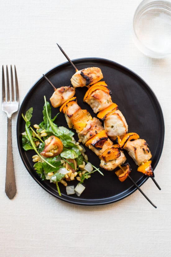 Two Mustard and Maple Pork Kebabs on a black plate with a salad.