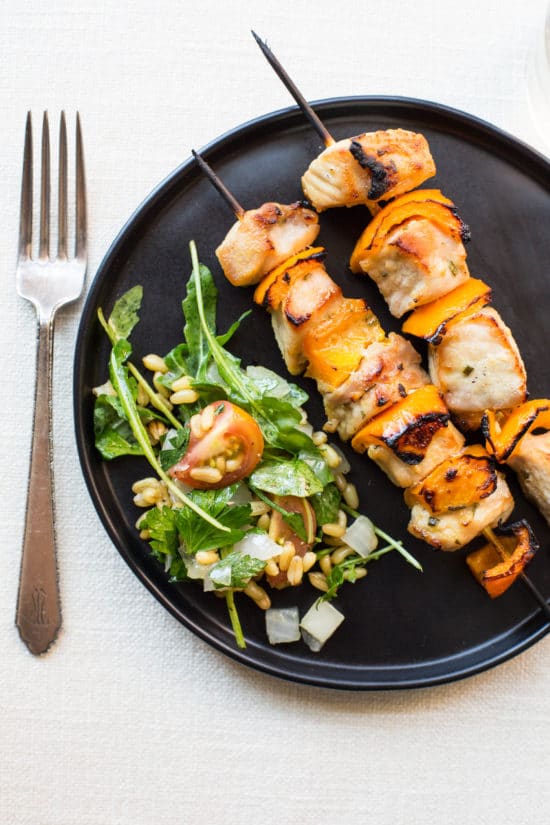 Black plate of Mustard and Maple Pork Kebabs with salad.