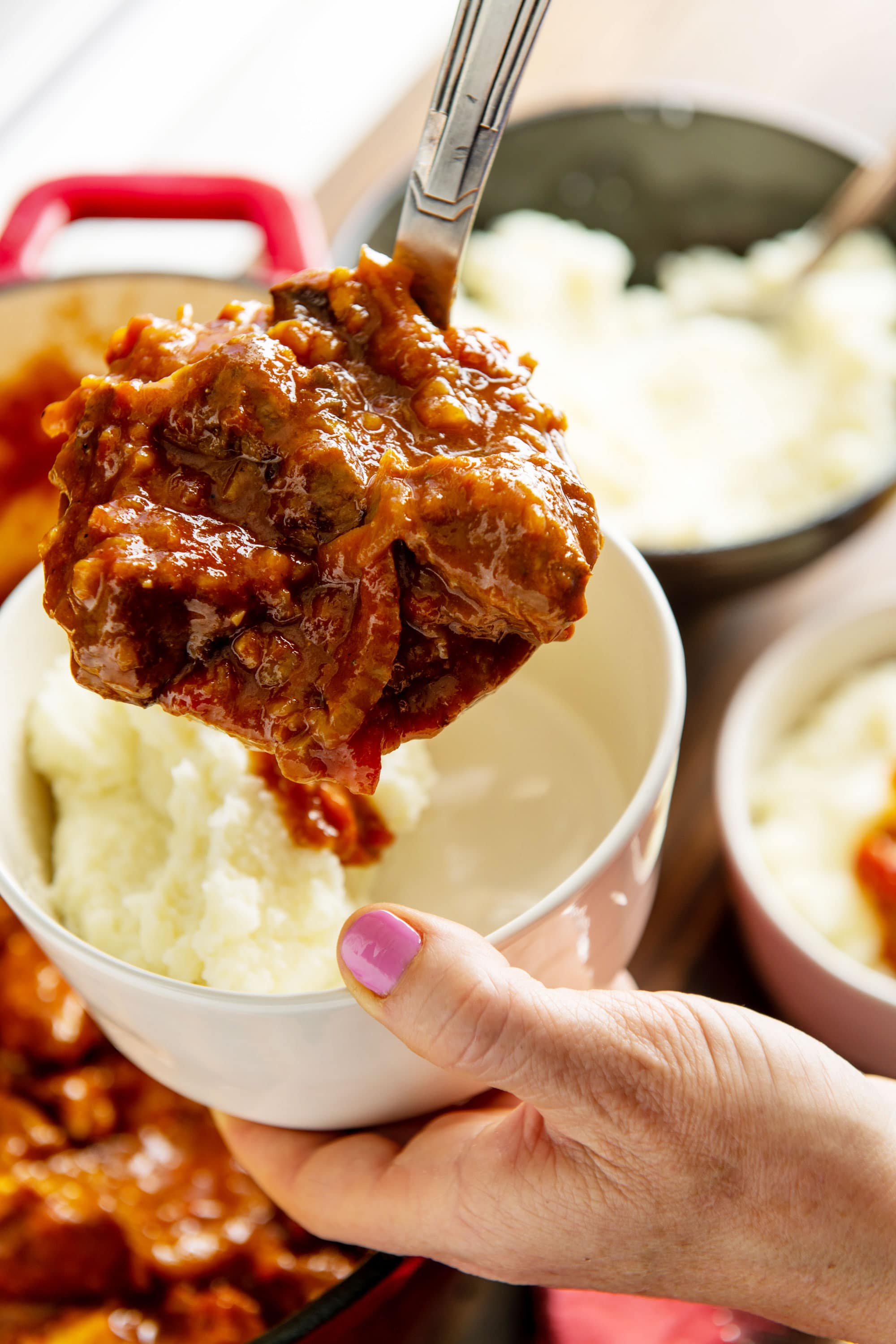 Woman scooping lamb stew over mashed potatoes in a white bowl.